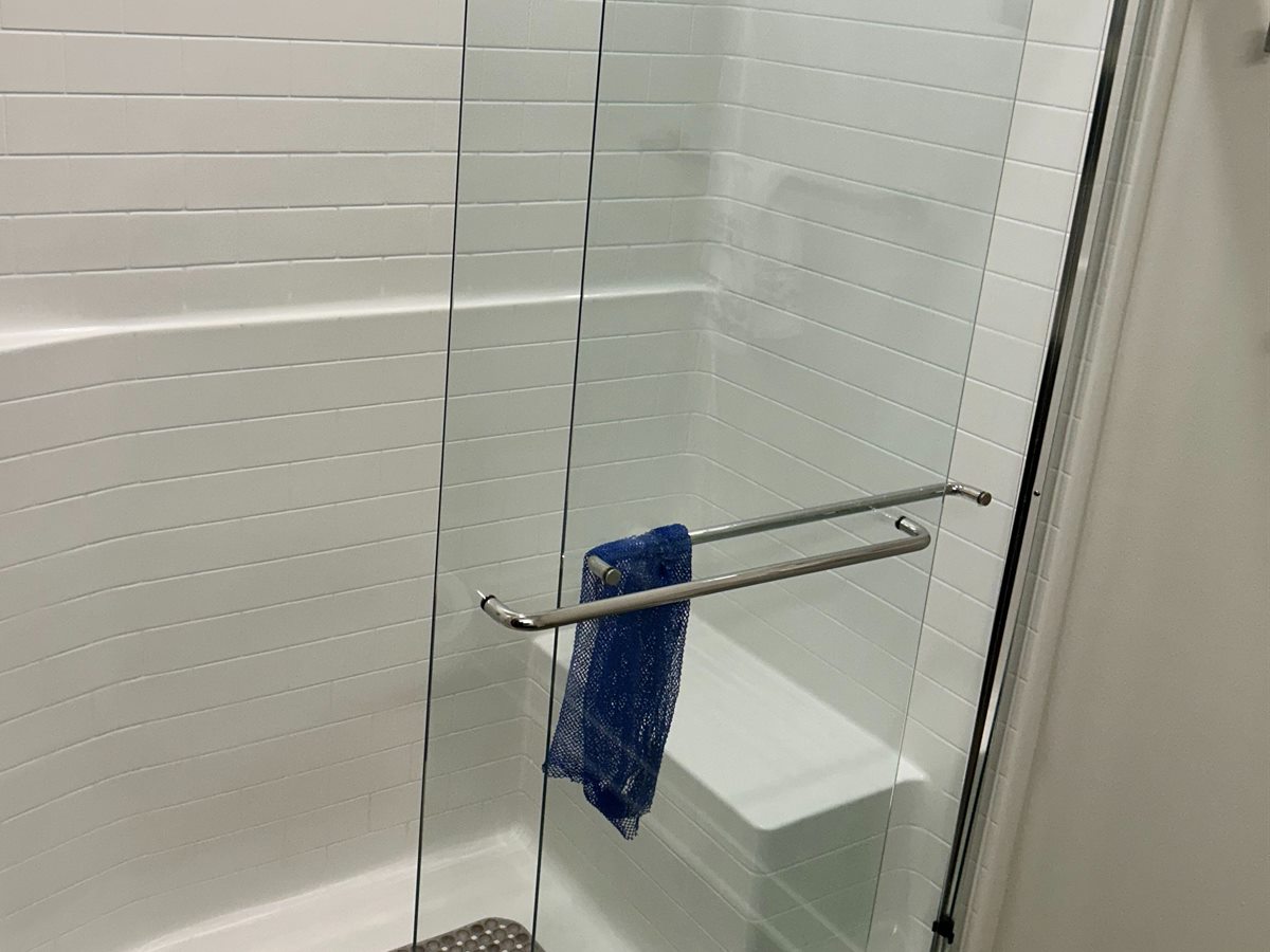 Scrubbed white tile shower, bench, and glass door after a deep clean